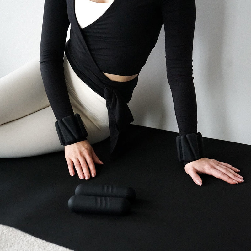 Pilates matil musta värvi käeraskusete ja 1 kg hantlitega.