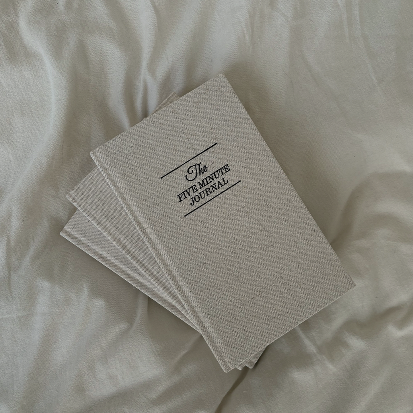 Kolm The Five Minute Journal päevikut valgetel linadel. 